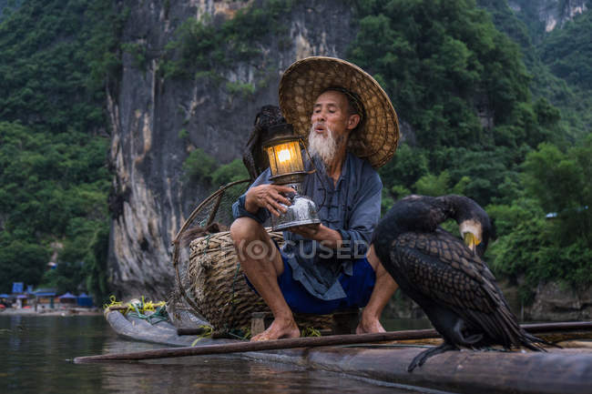 Рыбак-баклан на плоту держит фонарь — стоковое фото