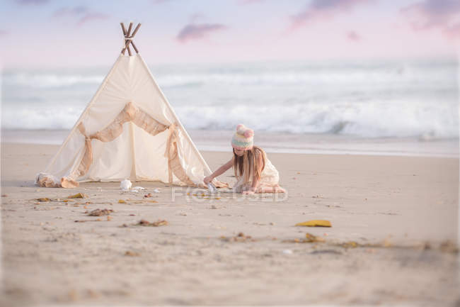 Girl sitting by wigwam on beach — Stock Photo