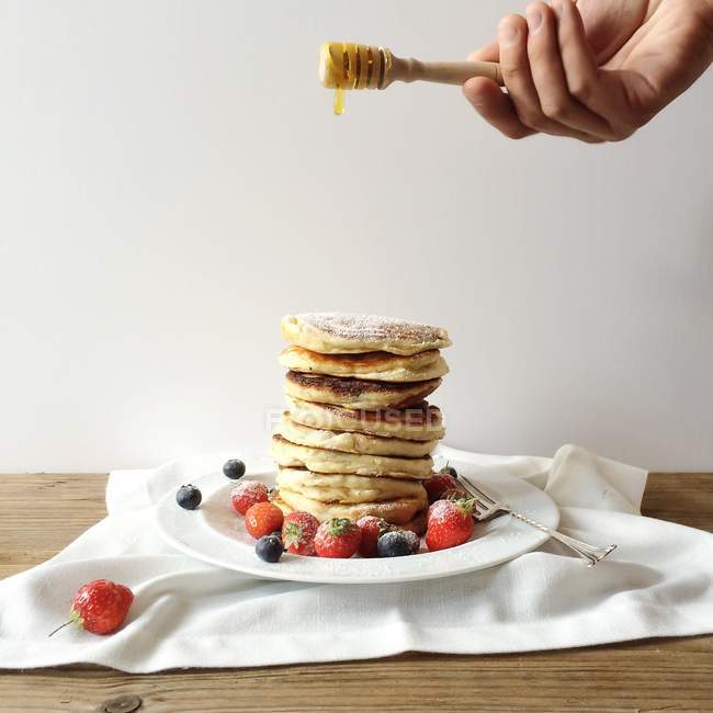 Man drizzling honey over stack of pancakes — Stock Photo