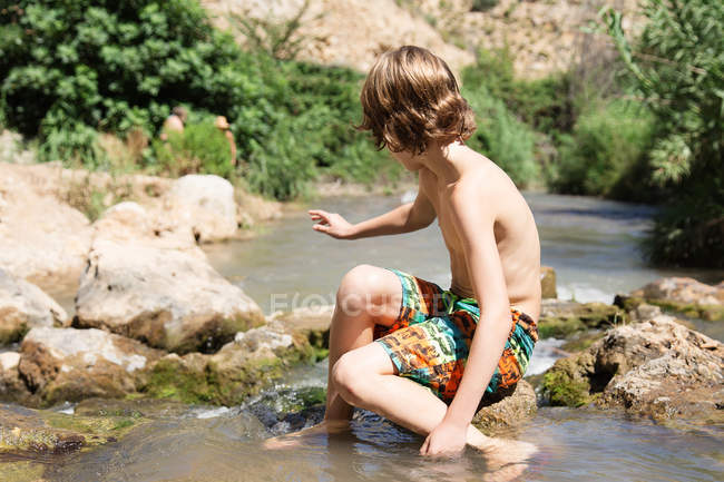 Niño sentado en la roca en el río - foto de stock