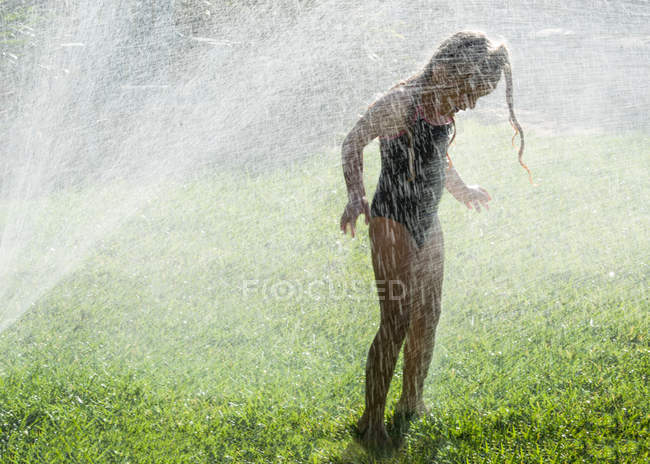 Girl playing in water sprinklers — Stock Photo
