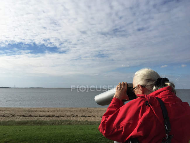 Donna sulla spiaggia guardando attraverso il binocolo — Foto stock