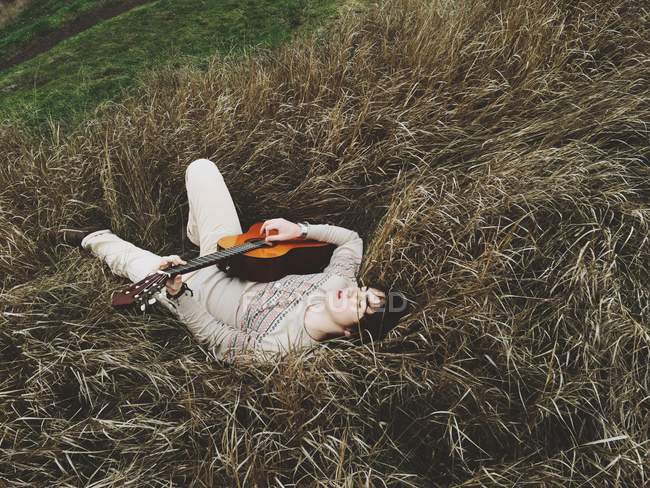 Niño acostado hierba con guitarra - foto de stock