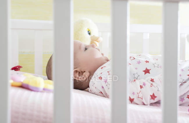 Bébé fille dans lit avec jouets autour — Photo de stock