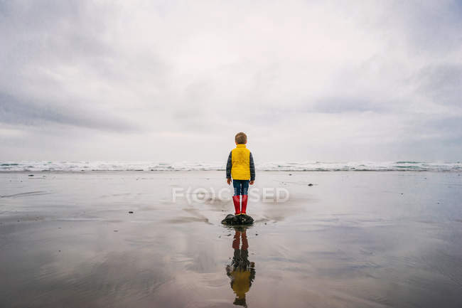 Boy standing on rock by sea — Stock Photo