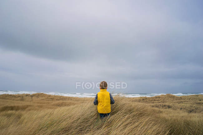 Garçon marchant à travers l'herbe vers l'océan — Photo de stock
