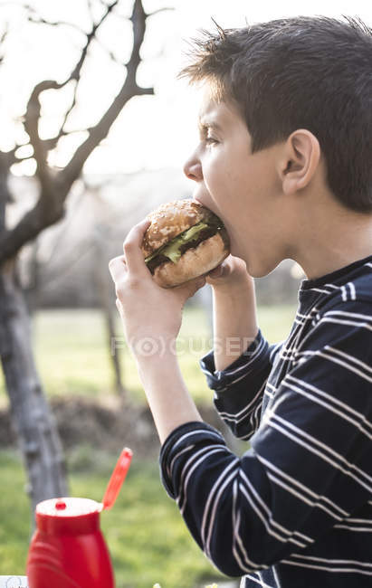 Junge isst Hamburger im Garten — Stockfoto