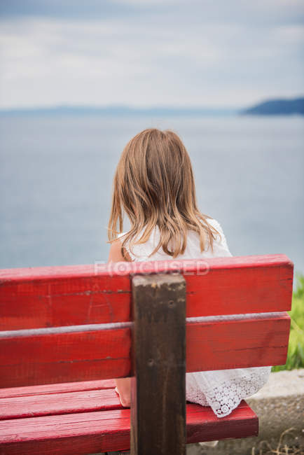Chica sentada en el banco mirando hacia el mar - foto de stock