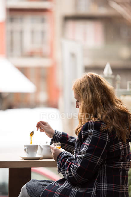 Femme mettant du miel dans une tasse — Photo de stock