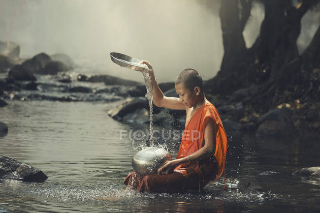 Начинающий монах сидит в ручье и охлаждается. — стоковое фото