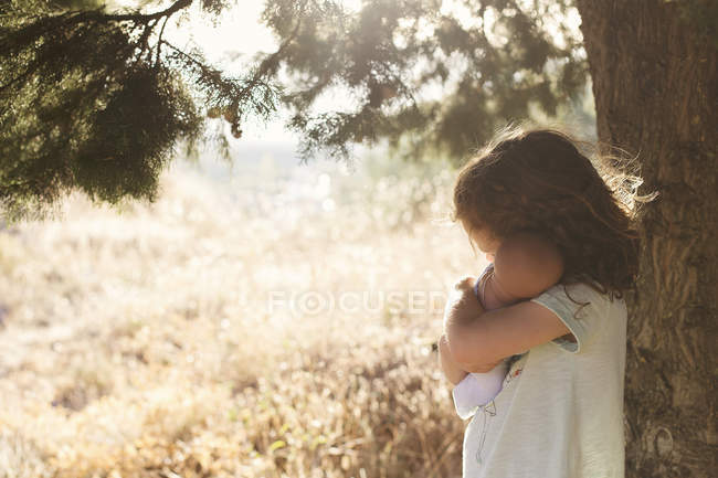 Chica en el campo abrazando muñeca - foto de stock