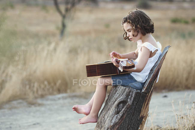 Дівчина сидить у полі граючи на гітарі — стокове фото