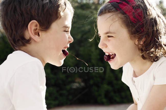 Мальчик и девочка лицом к лицу едят вишни — стоковое фото