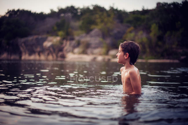 Niño de pie en el lago al atardecer - foto de stock