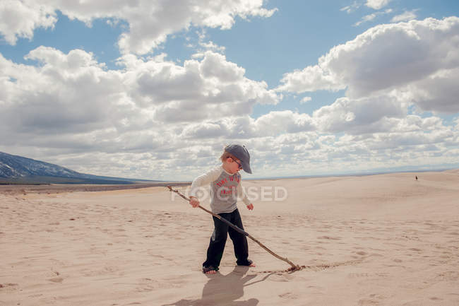 Niño escribiendo en arena con palo - foto de stock