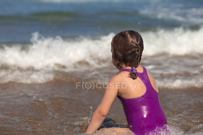 Ragazza seduta sulla spiaggia al bordo delle acque — Foto stock