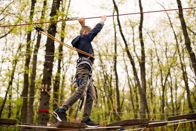 Menino em arnês de corda na plataforma de escalada — Fotografia de Stock