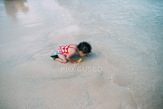 Дівчина сидить на пляжі, дивлячись на пісок — стокове фото