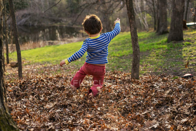 Хлопчик стрибає в стопці осіннього листя — стокове фото