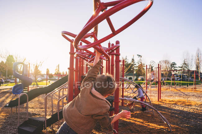 Rapaz balançando em barras de macaco — Fotografia de Stock