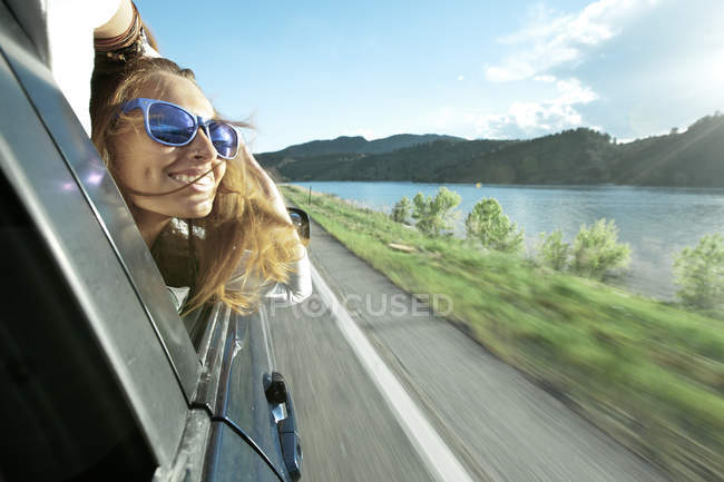 Mulher inclinada para fora da janela do carro enquanto dirige — Fotografia de Stock
