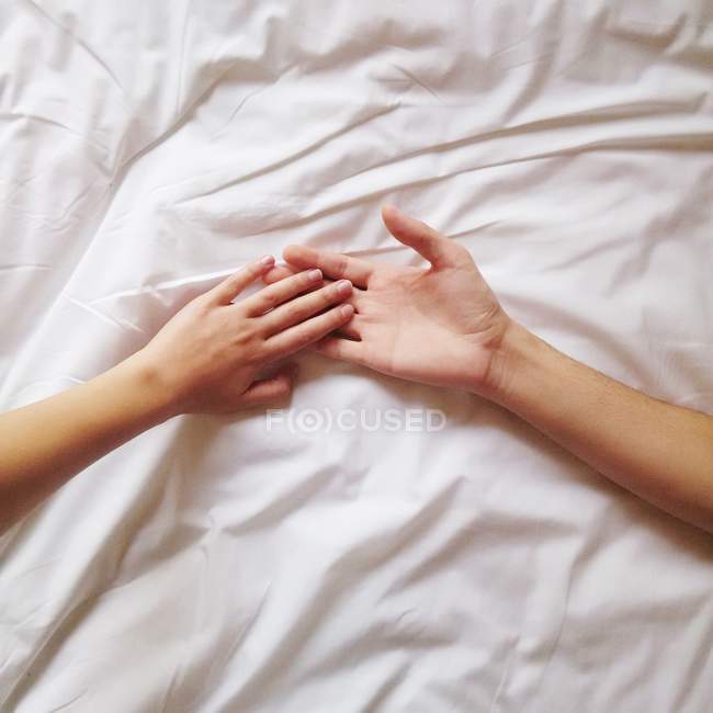 Пара лежащих в постели, держащихся за руки — стоковое фото