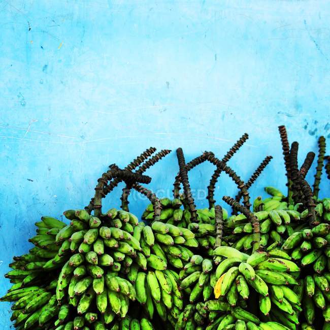 Stack of green bananas in front of blue wall — Stock Photo