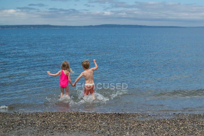 Vista posteriore di due bambini che corrono nell'oceano — Foto stock