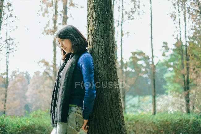 Femme réfléchie appuyé contre l'arbre dans la forêt — Photo de stock