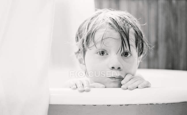 Vue rapprochée du mignon petit garçon regardant au-dessus du bord de la baignoire — Photo de stock