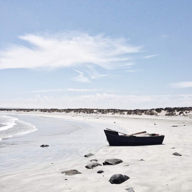 Barco abandonado en la playa contra la orilla del mar en un día soleado - foto de stock