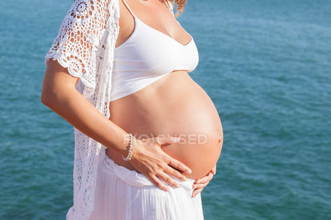 Geschnittenes Bild einer schwangeren Frau gegen das Meer — Stockfoto