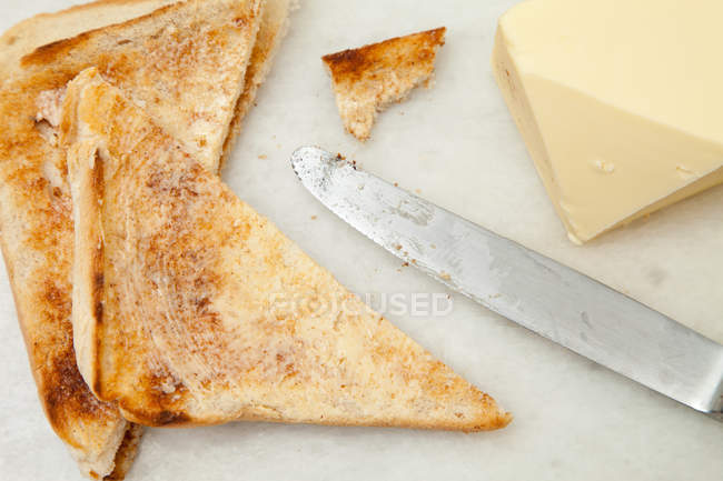 Vista superior de cerca de rebanadas de pan tostado y mantequilla con cuchillo - foto de stock