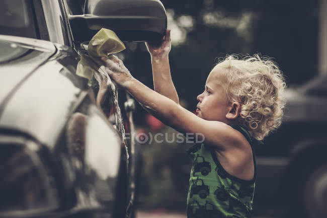 Side view of cute little boy with curly hair washing car — Stock Photo