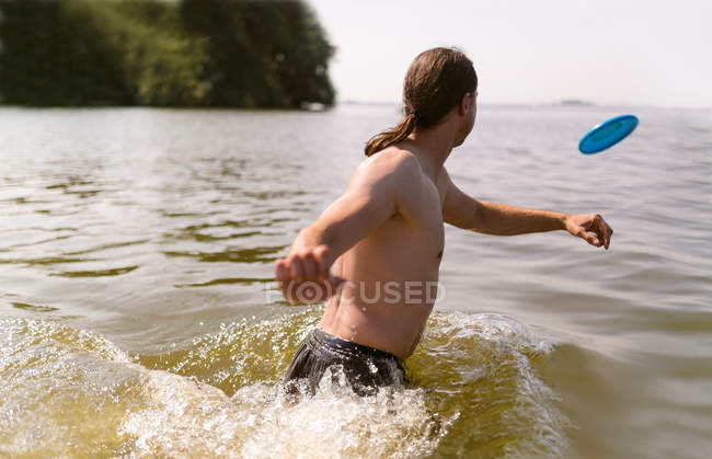 Чоловік грає з пластиковим літаючим диском в озері — стокове фото