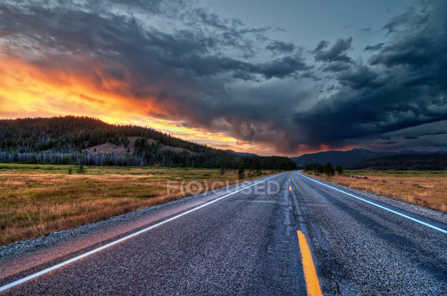 Vista panorámica de la carretera recta al atardecer bajo el cielo dramático - foto de stock