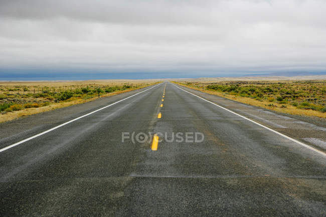 Blick auf leere Straße im Feld unter wolkenverhangenem Himmel — Stockfoto