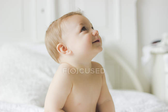 Портрет улыбающегося мальчика, сидящего на кровати в спальне — стоковое фото
