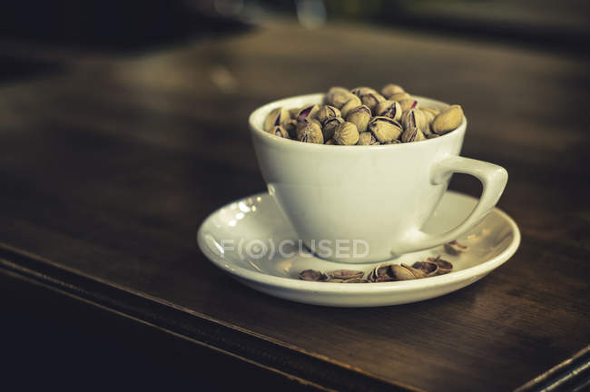 Pistachio nuts in a white cup on saucer — Stock Photo