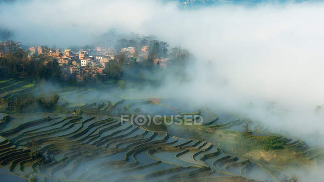 Vista panorâmica de campos de arroz em terraços e cidade coberta por névoa, Yunnan, China — Fotografia de Stock