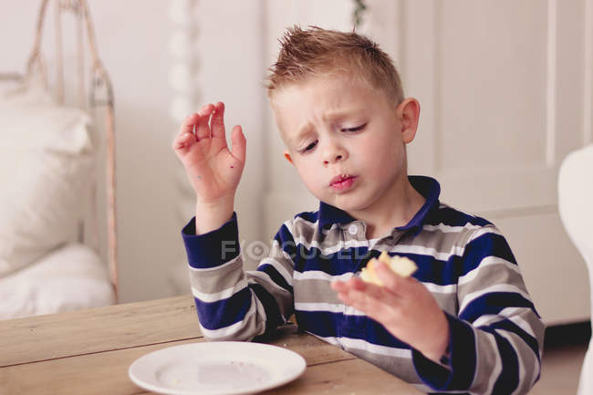 Мальчик ест сэндвич за деревянным столом — стоковое фото