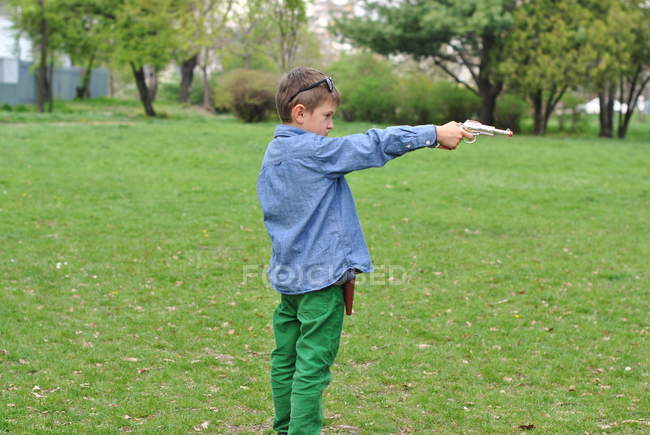 Menino brincando com uma arma de brinquedo no gramado — Fotografia de Stock