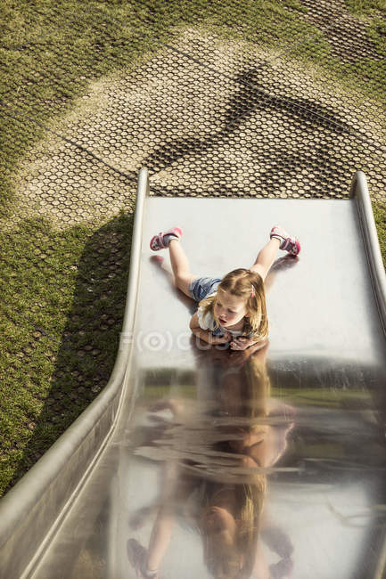 Вид сверху на девочку, лежащую на дне горки на детской площадке — стоковое фото