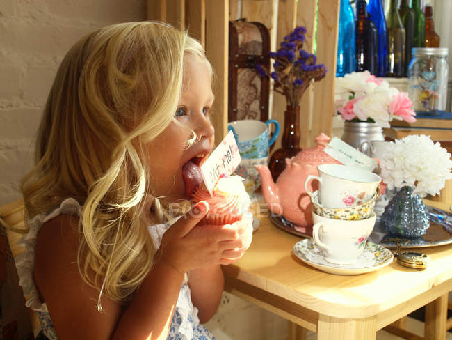 Beautiful blond little girl eating cupcake at tea party — Stock Photo