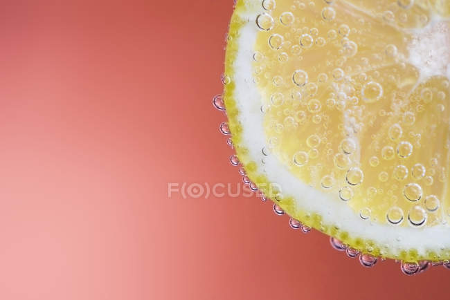 Primer plano de rodaja de limón con burbujas fondo rojo claro - foto de stock