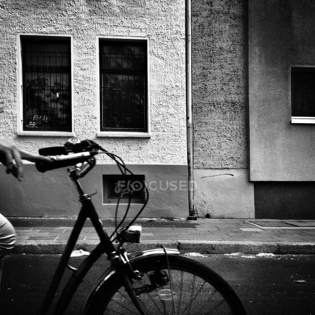 Mão humana segurando barra de alça de bicicleta na rua urbana com edifício no fundo — Fotografia de Stock
