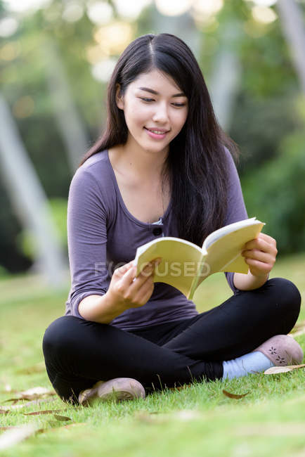 Улыбающаяся молодая женщина сидит в парке и читает — стоковое фото