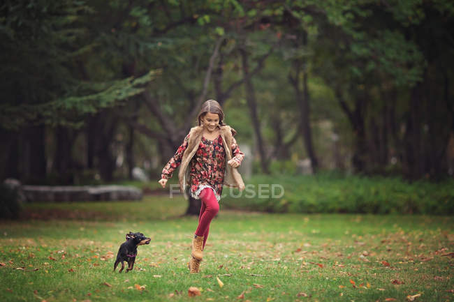 Girl chasing puppy dog in park — Stock Photo