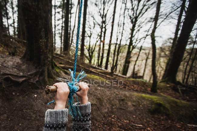 Крупным планом руки мальчика висят на веревке качели в лесу — стоковое фото