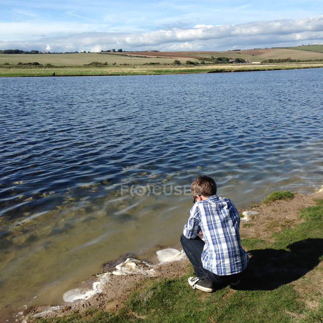 Хлопчик crouching на Ріверсайд та переглядають води — стокове фото
